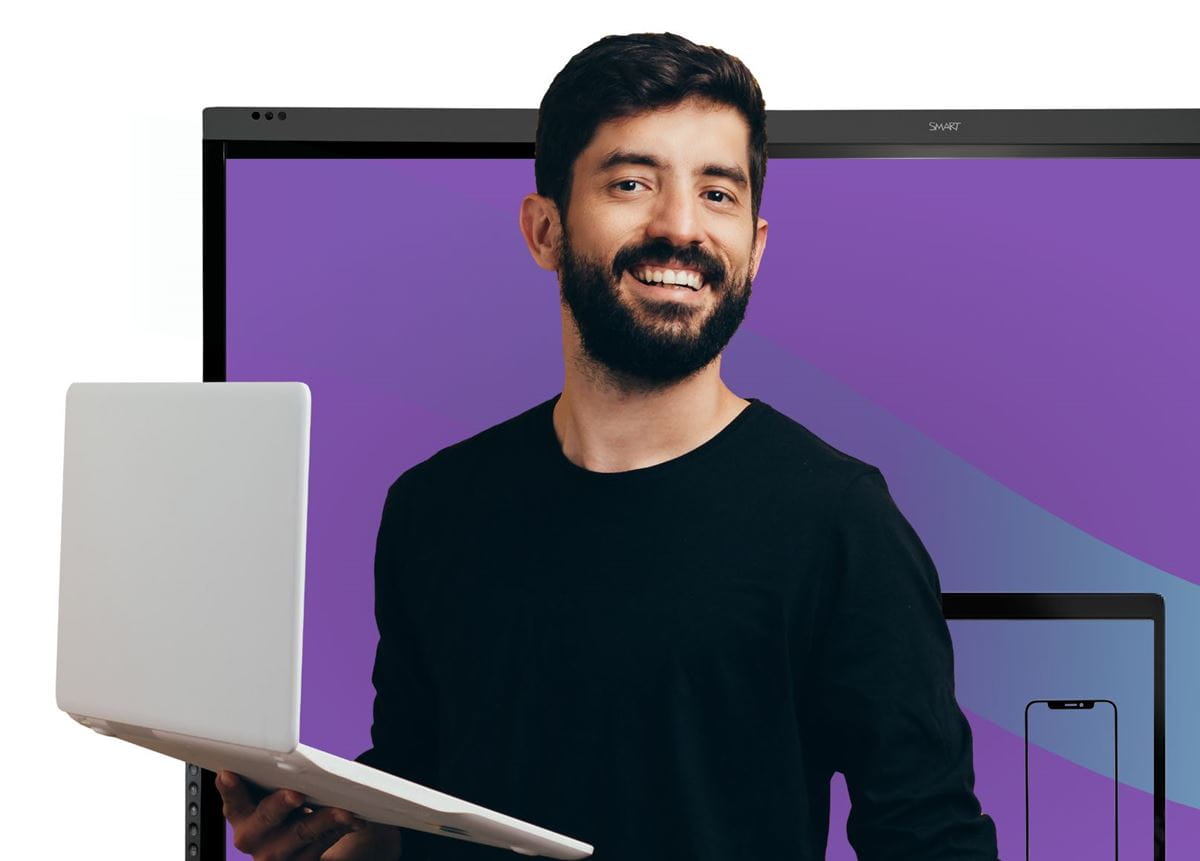 Business professional smiling and holding a laptop, standing next to a SMART interactive display in a business setting, representing SMART Remote Management.