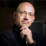 Close-up of José Luis Castaño Pérez looking contemplative, wearing glasses and a black shirt, resting his chin on his hand.