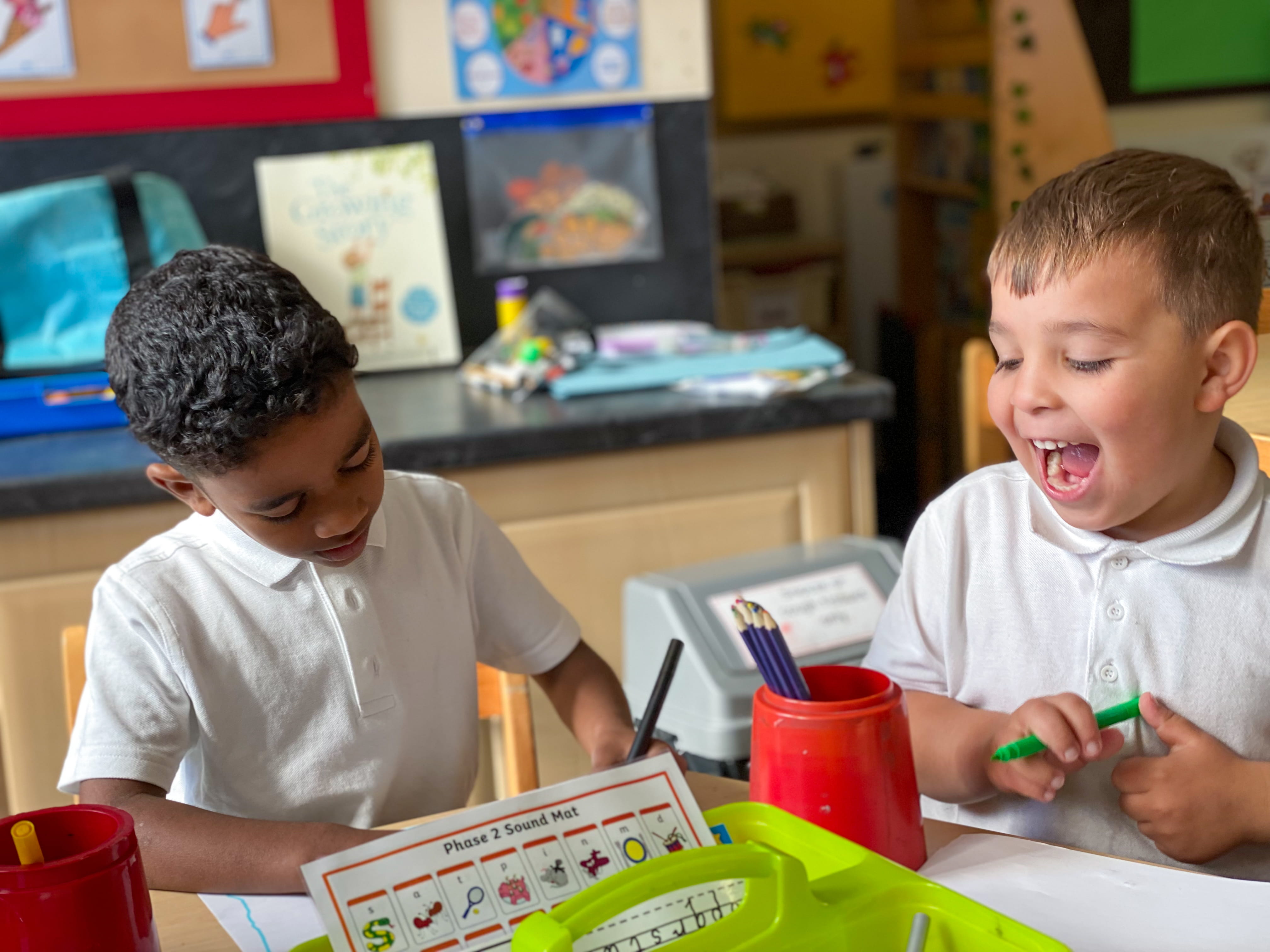 Two elementary students laugh as they work together on a classroom project.