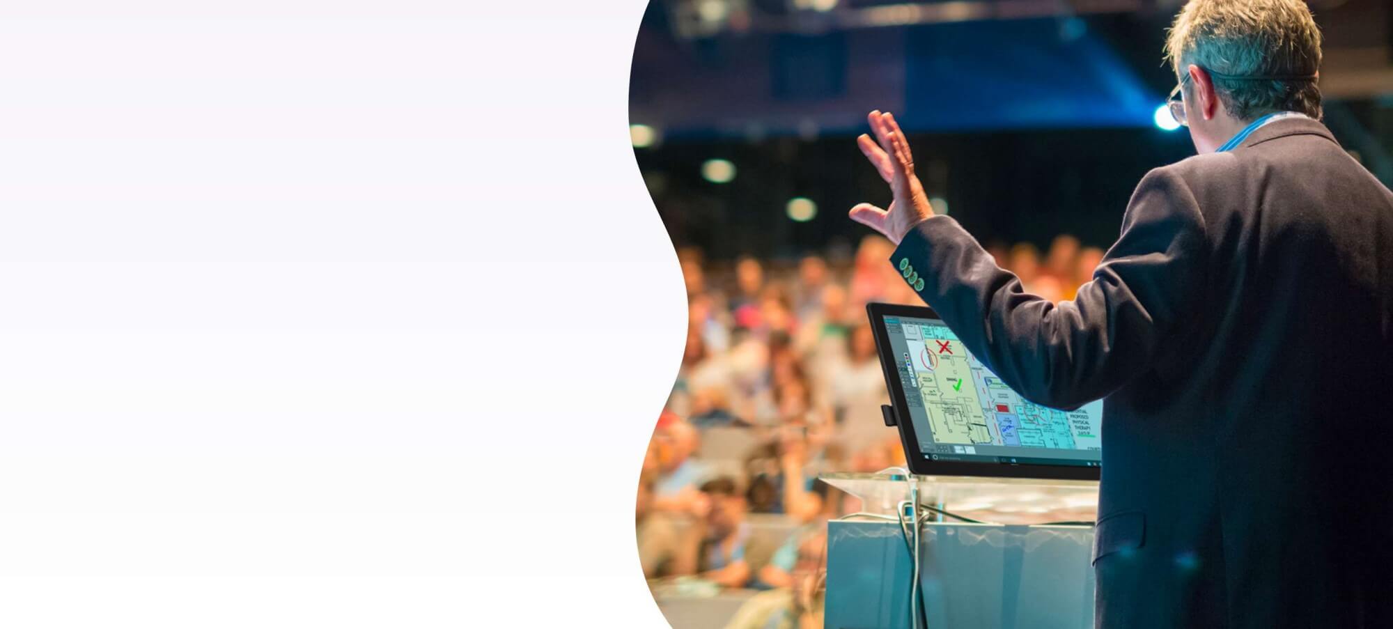A presenter is interacting with a SMART Podium 624 interactive display in front of an audience, highlighting the device's capability for making presentations interactive with touch, gestures, and digital ink.